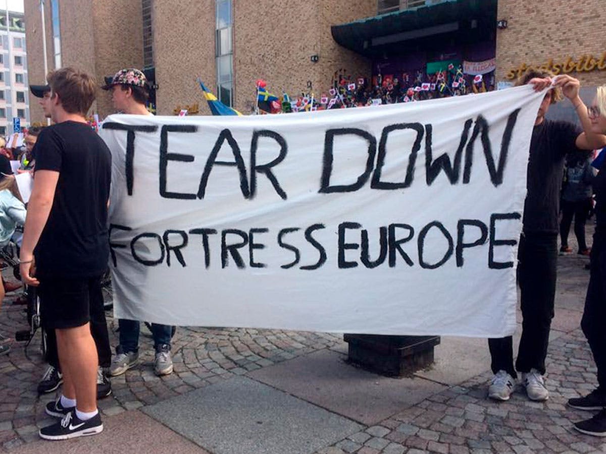 Two people in a demonstration, with a banner: 'Tear down fortress Europe'